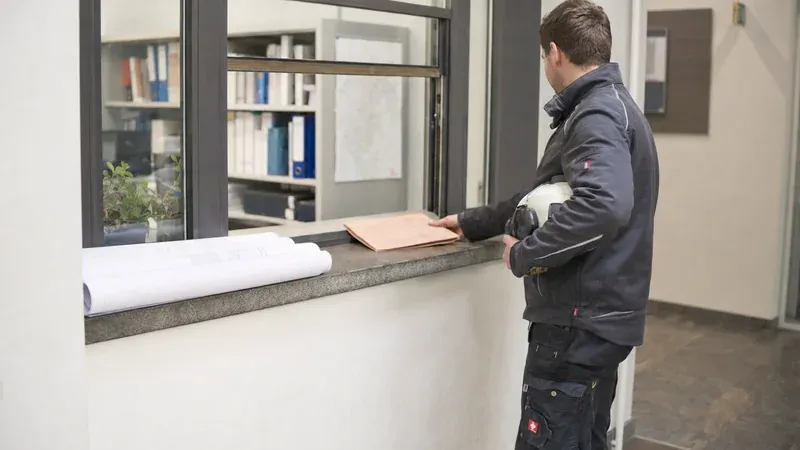 Handwerker holt Planrollen und Genehmigungsunterlagen am Bauamt ab
