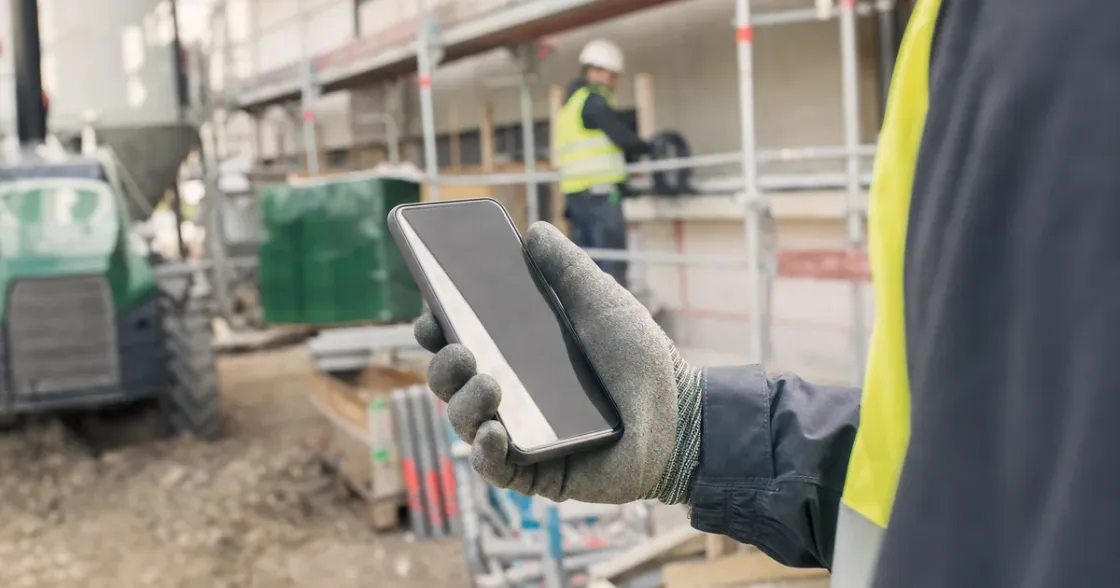 Handwerker prüft auf der Baustelle eine Benachrichtigung am Smartphone