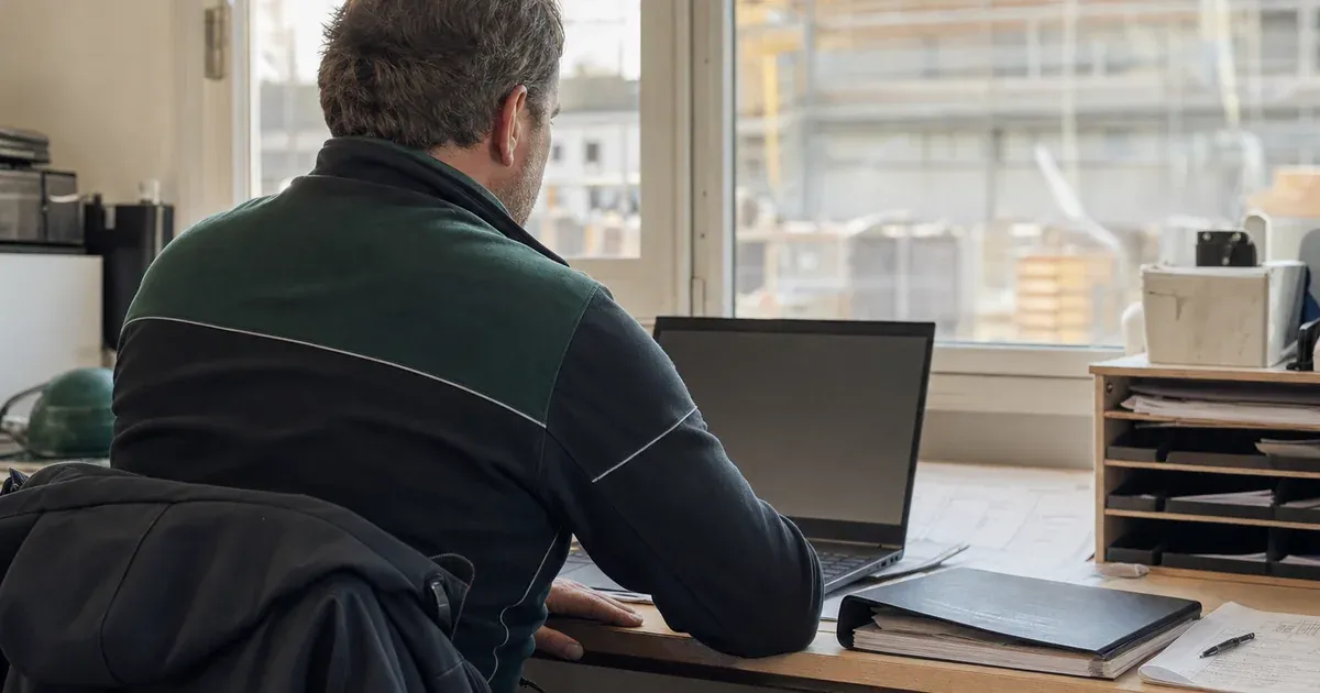 Bauunternehmer sichtet am Laptop im Baubüro Ausschreibungsunterlagen
